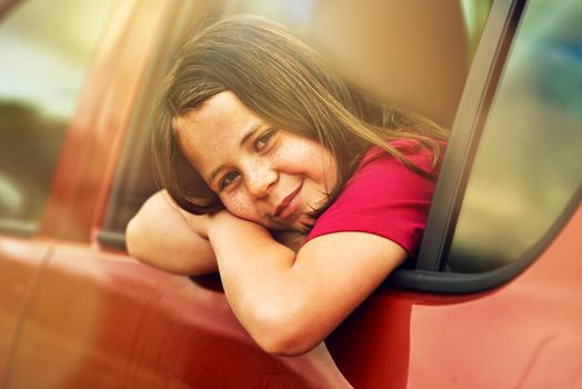 Those freckles will melt your heart. Portrait of an adorable little girl leaning out of a car window outside.
