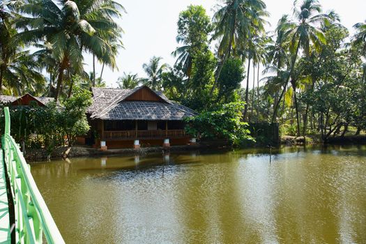Idyllic tranquility. Traditional wooden building surrounded by tropical palm trees on the banks of a river in India.