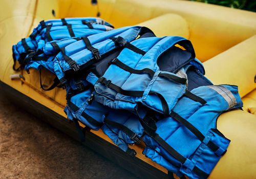 These guys can save your life. Shot of a pile of river rafting life jackets lying on top of a rubber river rafting boat outside during the day.