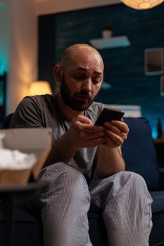 Depressed man using smartphone to browse internet at home