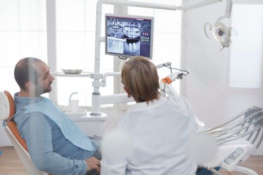 Patient with toothache sitting on dental chair looking at teeth radiography discussing dentistry treatment with stomatologist doctor during medical consultation in dental office. stomatology Concept
