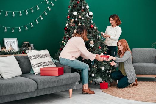 Gather round. Shot of three attractive women decorating a Christmas tree together at home.