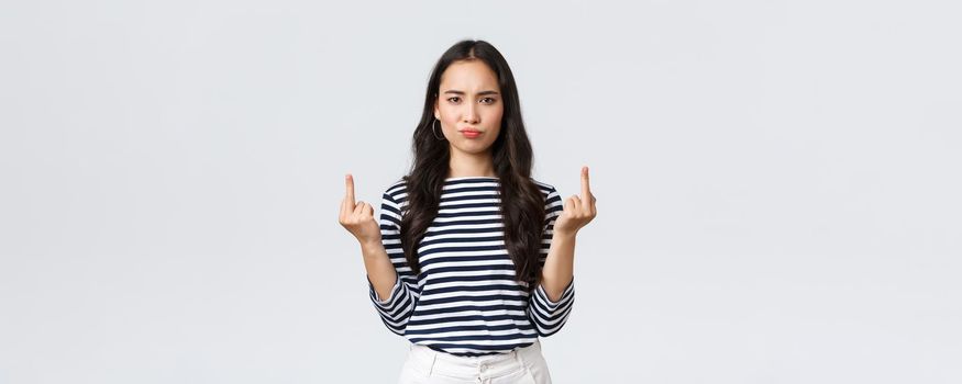Lifestyle, beauty and fashion, people emotions concept. Pouting bothered young pissed-off asian female look annoyed and showing middle-fingers rude gesture, white background.