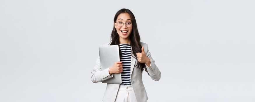 Business, finance and employment, female successful entrepreneurs concept. Young confident businesswoman in glasses, showing thumbs-up gesture, hold laptop, guarantee best service quality