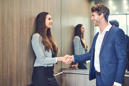 Its a pleasure meeting you. Cropped shot of a businessman and businesswoman greeting by handshake in an elevator.