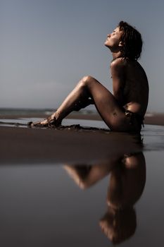 Sexy female body covered with sand. Girl on a beach with sea water reflection. .