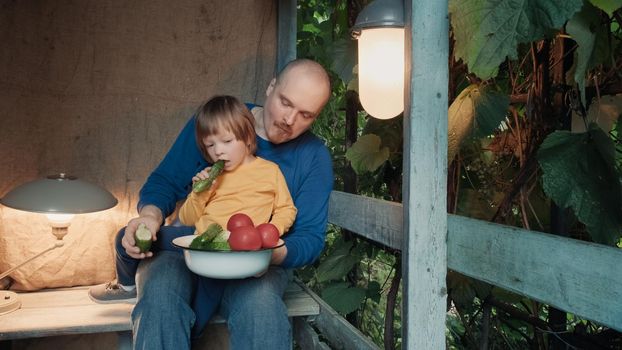 Father and small child eat fresh, organic vegetables from farm sitting on porch