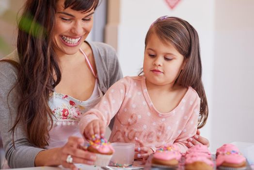 Adding some sprinkles to top it all off. Cropped shot of a little girl baking together with her mother at home.
