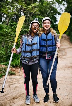 We are ready to go rafting again. Portrait of two cheerful young women wearing protective gear while holding a rowing paddle outside during the day.