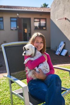 Double the cuteness out here. Portrait of a happy little girl sitting on a chair and holding her pet dog outdoors.