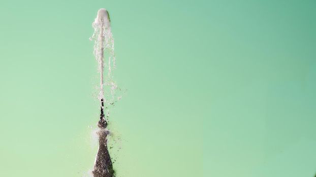 Fountain with shining clear liquid on a pale emerald background