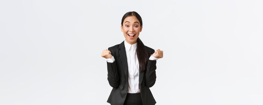 Relieved happy female office manager, successful businesswoman achieve goal, winning and feeling rejoice, fist pump and shouting yes satisfied, standing white background upbeat