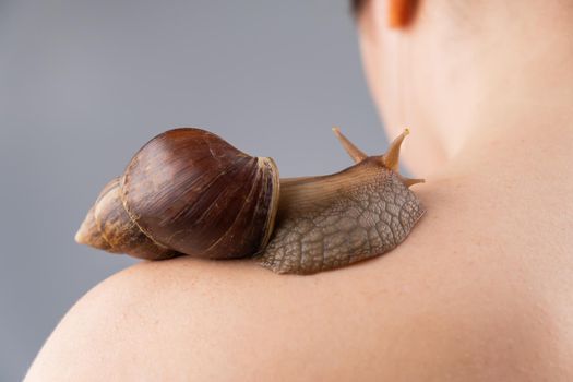 Close-up of a snail crawling over the head of a woman's shoulder. Skin care