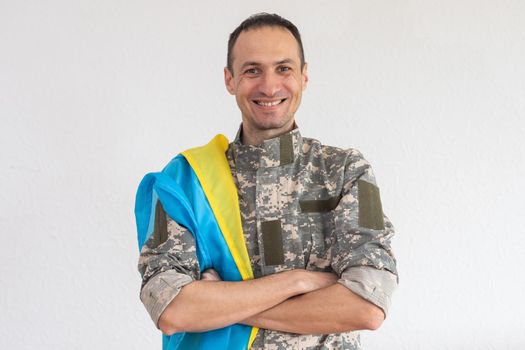 Ukrainian man warrior dressed in a military pixel uniform holds the yellow-blue flag of the state of Ukraine and on the chain a small coat of arms of the country of trident, close up.