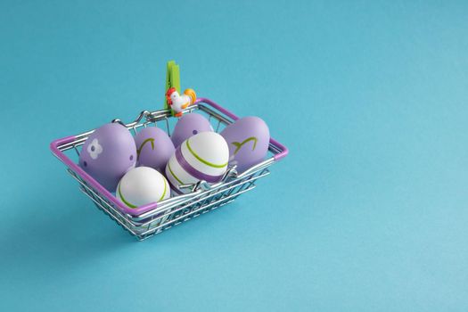 Metal shopping basket with lilac chicken eggs on a blue background. Dietary fresh product