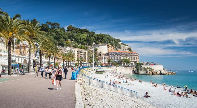 France, Nice, 15 May 2017: Promenade Anglais, Beautiful Public Beach, Tourists, Sunbath People, Swim, Sunny Day, People sit on the well-known blue chairs