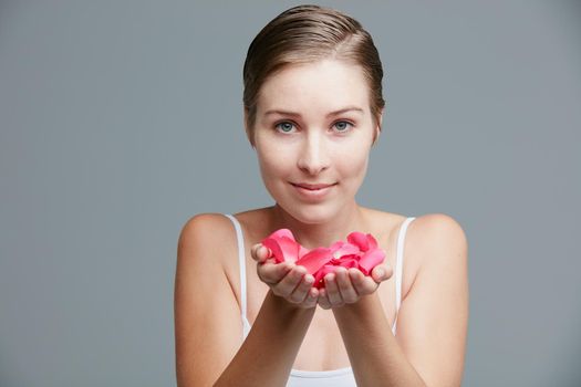 Beauty inspired by the softness of petals. Studio portrait of an attractive young woman holding a handful of pink petals against a gray background.