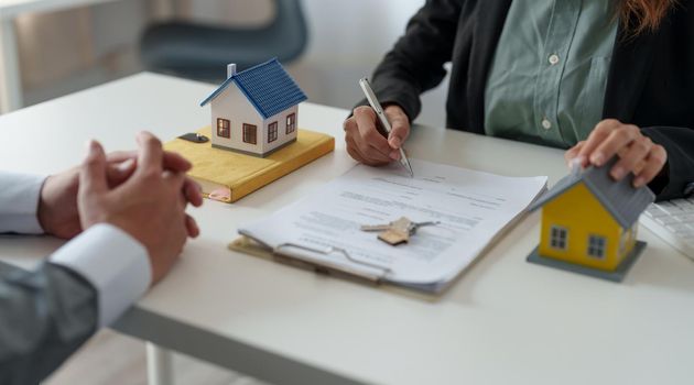 Real estate agent assisting client to sign contract at desk with house model