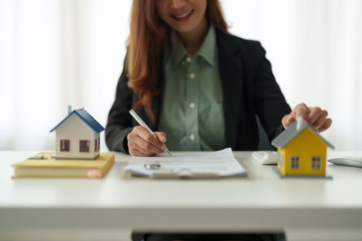 Asian business woman signs contract behind home architectural model - Real estate concept
