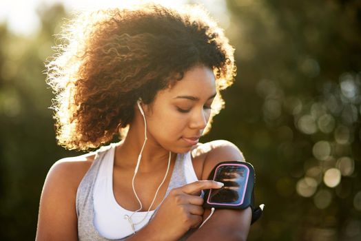 Pick the playlist that gets you going. Shot of an attractive young woman listening to music while exercising outdoors.