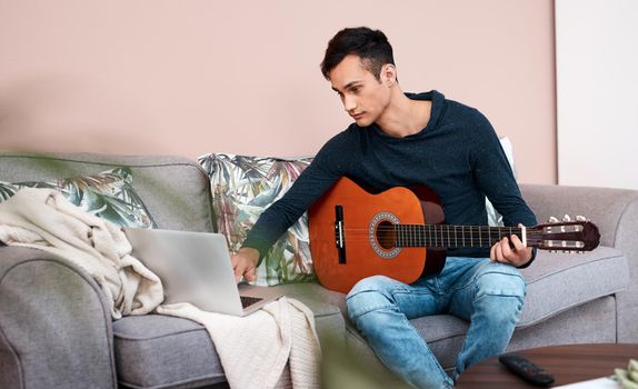 What lessons has lockdown taught you. Shot of a young man using a laptop while playing the guitar at home.