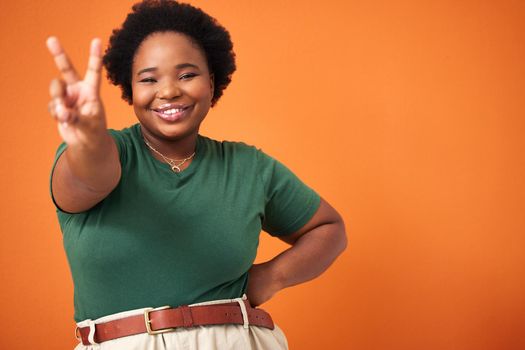 We spread peace and positivity over here. Shot of a beautiful young woman showing the peace sign while standing against an orange background.
