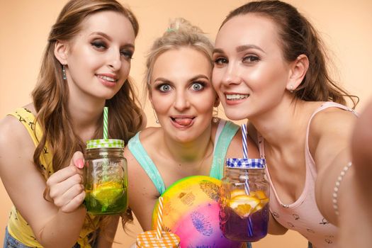 Sweet Life. Three beautiful slender women in summer clothes with cocktails are laughing, having a good time together. Studio, isolated background. The concept of recreation