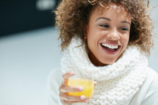 Keeping winter colds and flu at bay the citrusy way. Shot of a young woman dressed in warm clothing drinking a glass of orange juice.