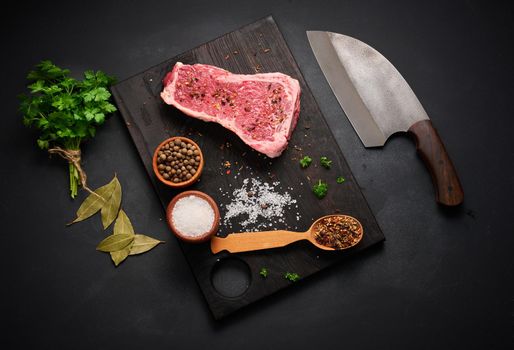raw piece of beef meat, striploin steak on a black background, top view. Marbled piece of meat New York