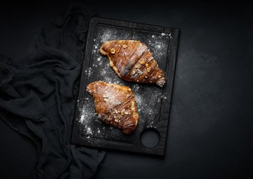 baked croissants on a black wooden board sprinkled with powdered sugar