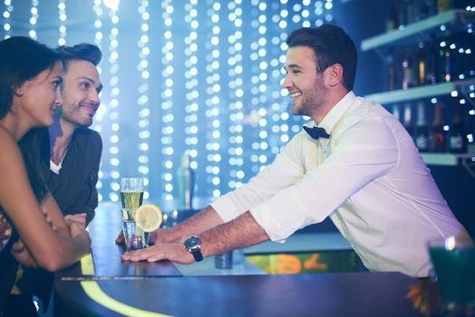 Drinks for the happy couple. Shot of a happy bartender serving drinks to a couple in a nightclub.
