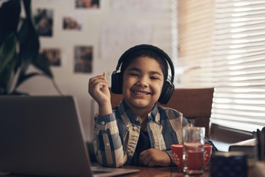 Break time is snack time. Shot of an adorable little boy using a laptop and headphones while completing a school assignment at home.