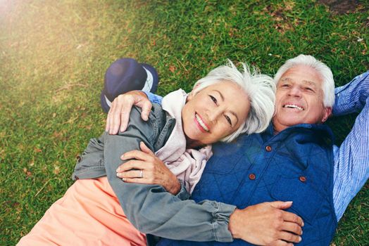 Everyday I fall in love with him all over again. Portrait of a happy senior couple lying down on the grass together in the park.