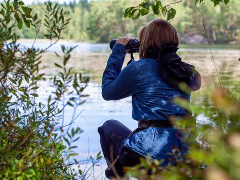 Young woman looking through binoculars at birds on the lake. Birdwatching, zoology, ecology. Research in nature, observation of animals Ornithology autumn bird migration selective focus, soft focus