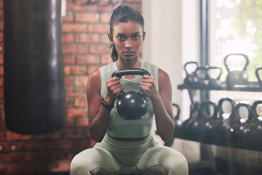 I came here to crush some goals. Shot of a young woman working out with a kettle bell in a gym.
