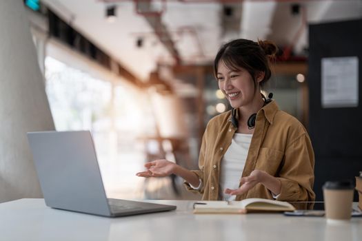 smiling asian woman freelancer wearing headset, communicating with client via video computer call. Millennial pleasant professional female tutor giving online language class.