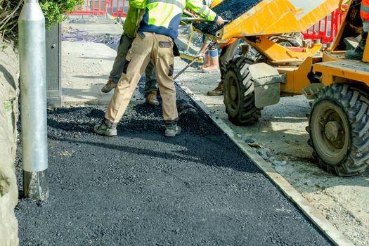 Construction workers placing hot tarmac during roadworks and footpath repair