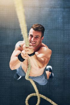 Theres no room for the weak in here. Shot of a muscular young man climbing a rope at the gym.