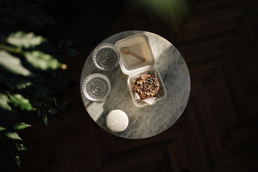 Top view of Chocolate bento cake in eco box with wooden spoon. White candle and chmpagne glasses on luxury marble table