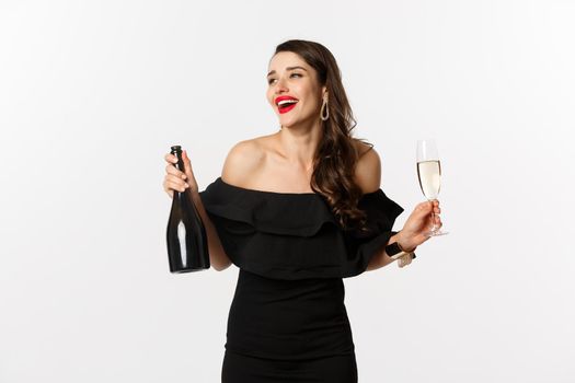 Celebration and party concept. Stylish brunette woman in glamour dress holding bottle and glass of champagne, having fun on new year holiday.