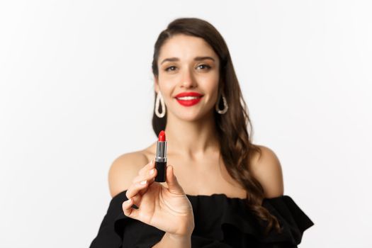 Fashion and beauty concept. Beautiful woman in black dress showing red lipstick and smiling, standing over white background