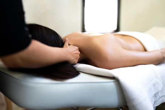 Unrecognizable massage therapist giving neck massage to female client.