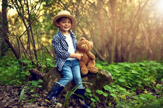 Theres no better companion in the woods. Shot of a little boy sitting in the forest with his teddy bear.