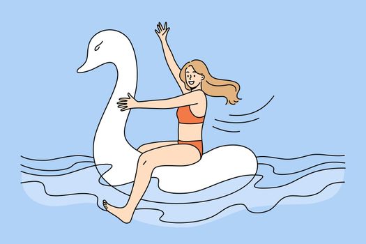 Happy girl in swimsuit float on rubber swan