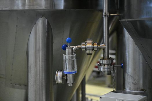 Photo of a valve tap against the background of large stainless steel tanks for a beer production