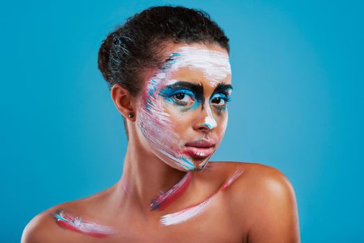 Bright, bold and beautiful. Studio portrait of a beautiful young woman covered in face paint posing against a blue background.