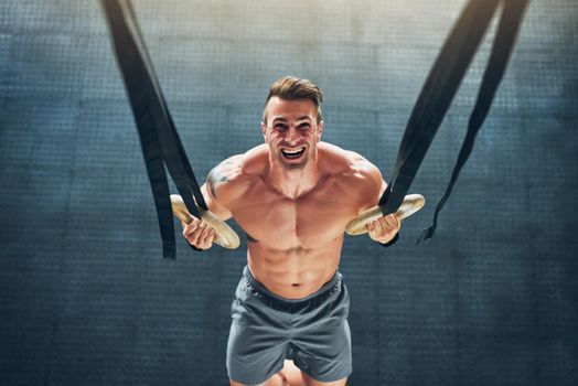Burn and firm. Shot of a muscular young man working out with gymnastic rings at the gym.