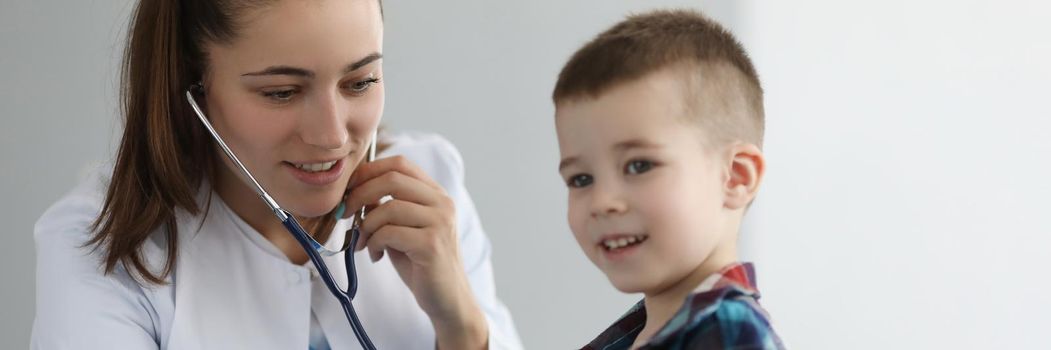 Doctor pediatrician listening to heart with stethoscope to little boy in clinic