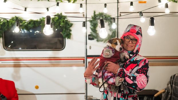 Caucasian woman holding Jack Russell Terrier dog by the trailer. Christmas van decorated