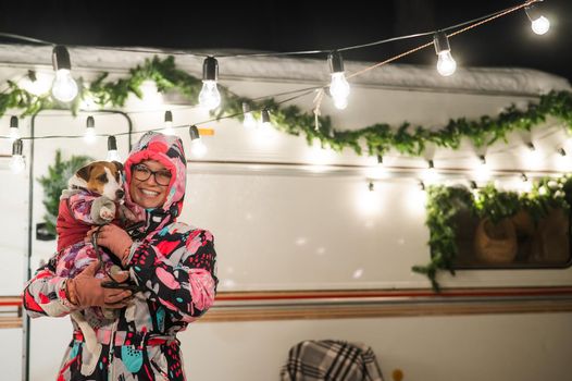 Caucasian woman holding Jack Russell Terrier dog by the trailer. Christmas van decorated